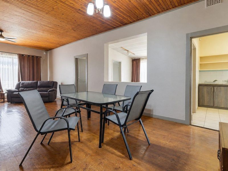 Open-plan living and dining area featuring timber ceilings, laminate flooring, and a convenient pass-through window connecting to the adjacent scullery.
