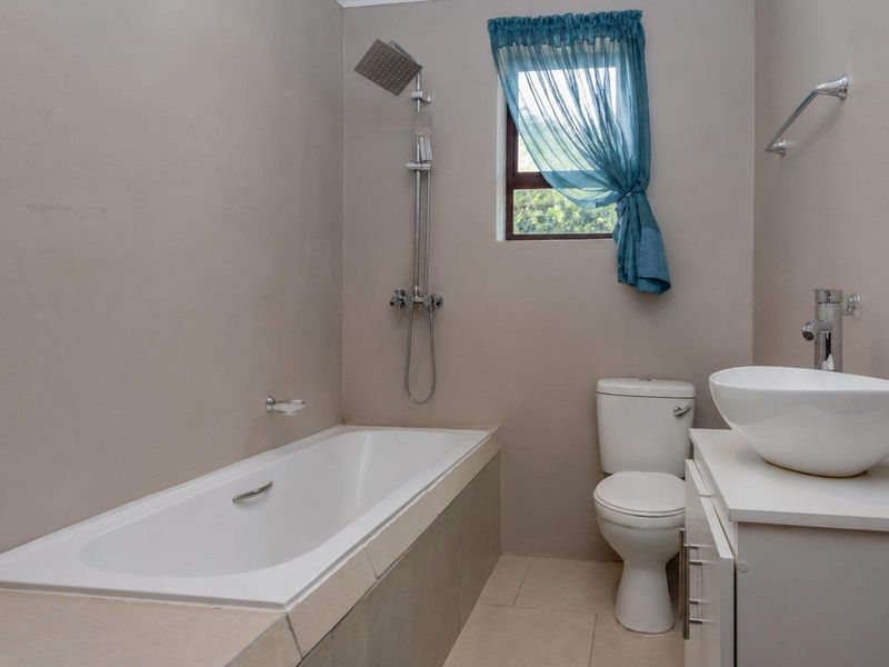 A functional bathroom featuring a built-in bathtub with shower attachment, a modern vessel sink on a vanity cabinet, and a standard toilet.
