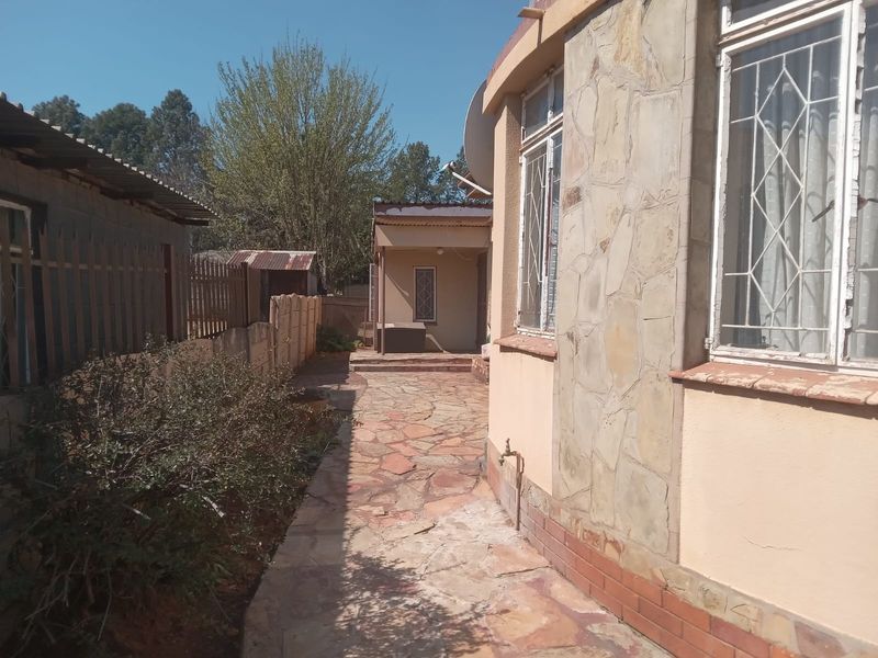 A side view of the property featuring stone cladding, a paved walkway, and security bars on the windows.