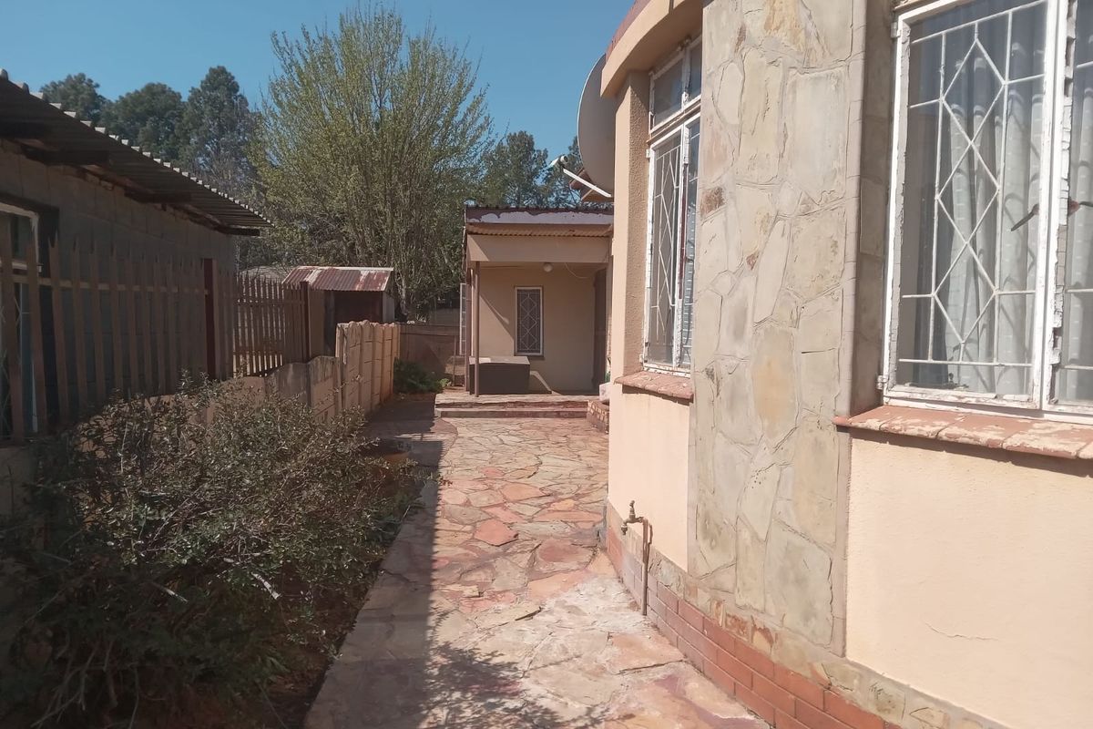 A side view of the property featuring stone cladding, a paved walkway, and security bars on the windows.