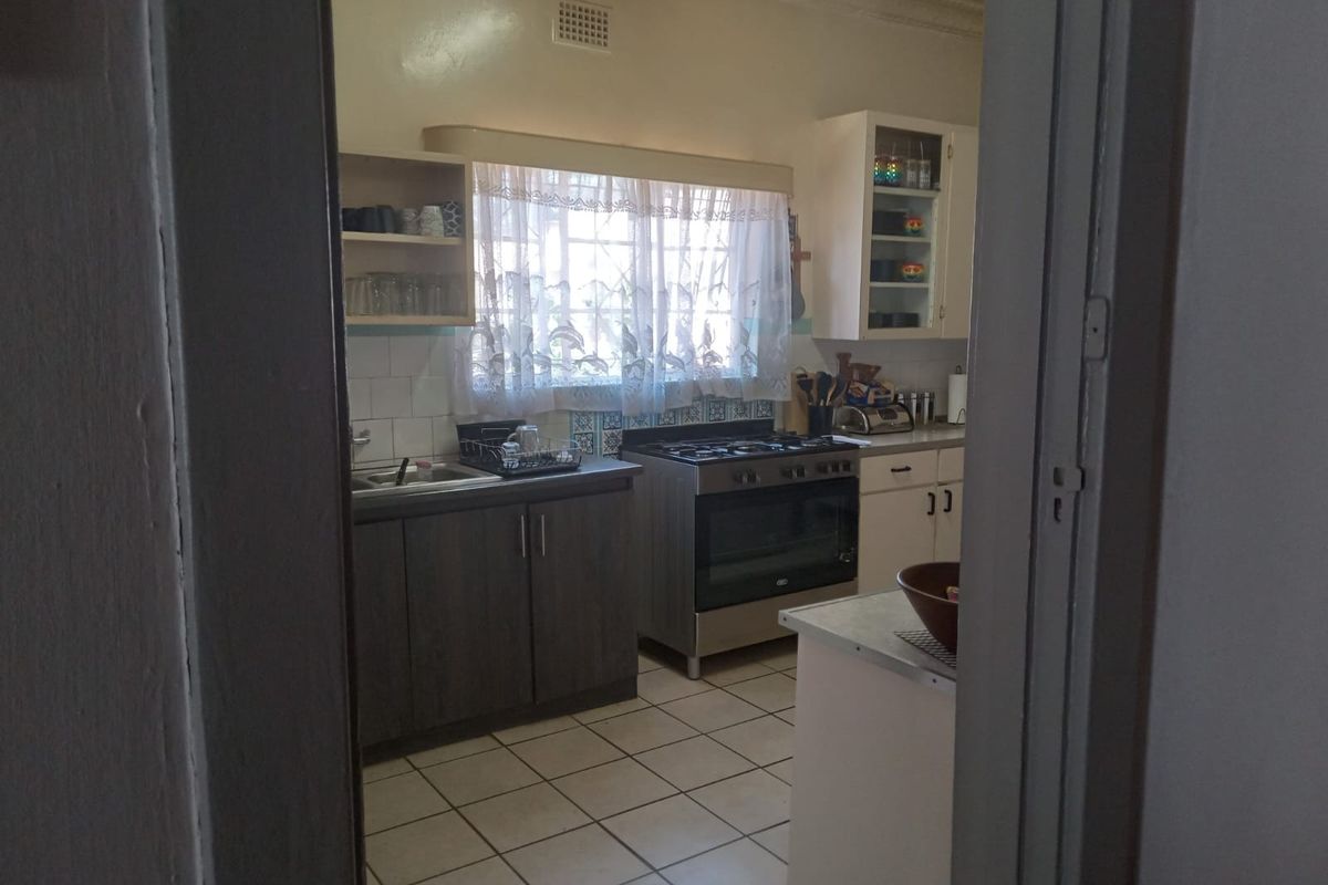 A functional kitchen featuring built-in cabinetry, a gas stove with oven, tiled backsplash, and tiled flooring, viewed through a doorway.
