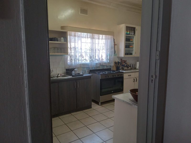 A functional kitchen featuring built-in cabinetry, a gas stove with oven, tiled backsplash, and tiled flooring, viewed through a doorway.