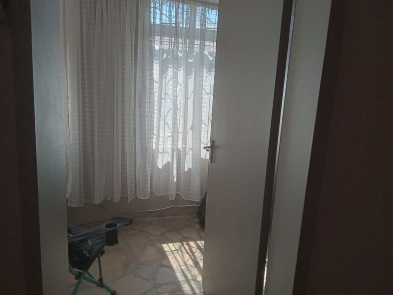 A simple bedroom space featuring tiled flooring and a window with security bars, viewed through an open doorway.