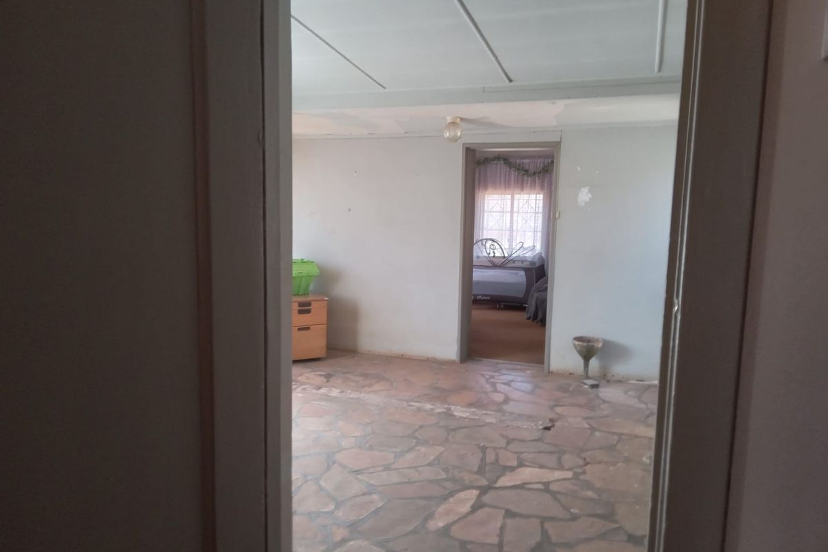 An empty living area featuring traditional stone flooring and ceiling panels, requiring cosmetic updates and wall repairs.