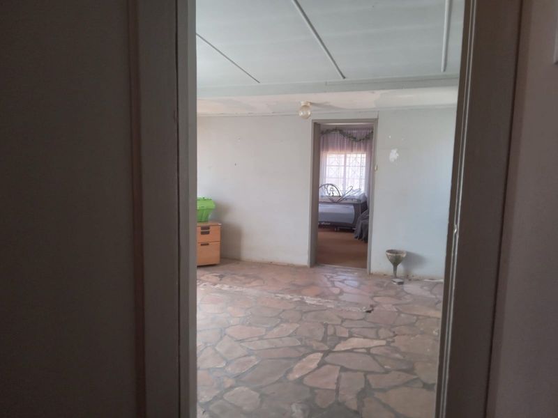 An empty living area featuring traditional stone flooring and ceiling panels, requiring cosmetic updates and wall repairs.