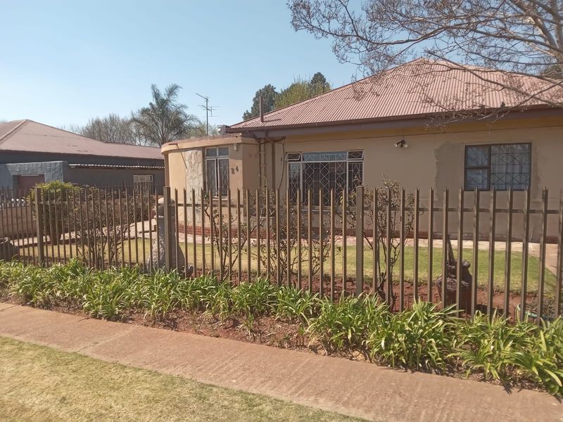 Front view of a single-story house featuring a metal roof, security fencing, and a landscaped garden area.