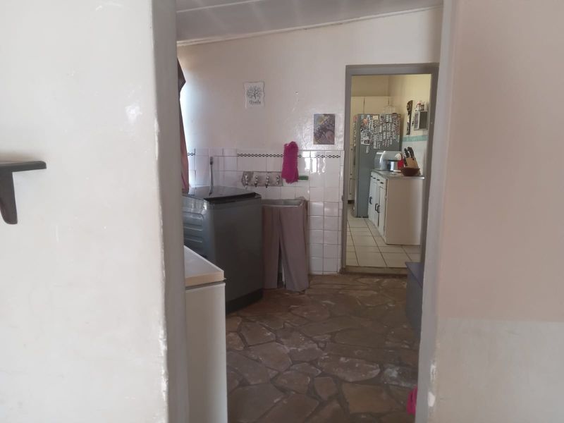A functional laundry area featuring stone flooring and a tiled splashback, with a view through to the adjacent kitchen space.