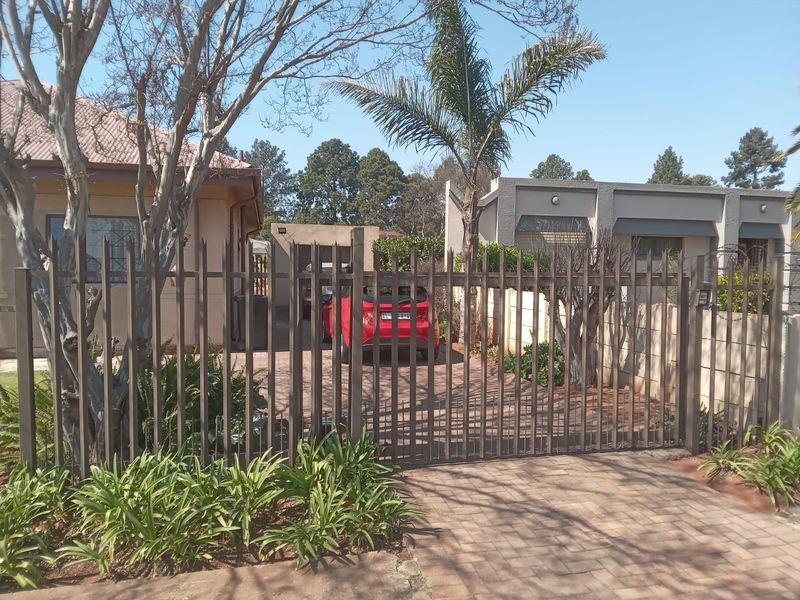 Front view of the property featuring a paved driveway, metal security gate, and boundary wall with security spikes.