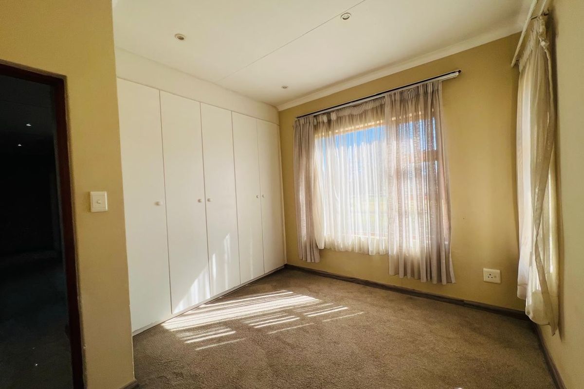 A bright, empty bedroom featuring neutral wall tones, carpeted flooring, and ample built-in cupboard storage space.