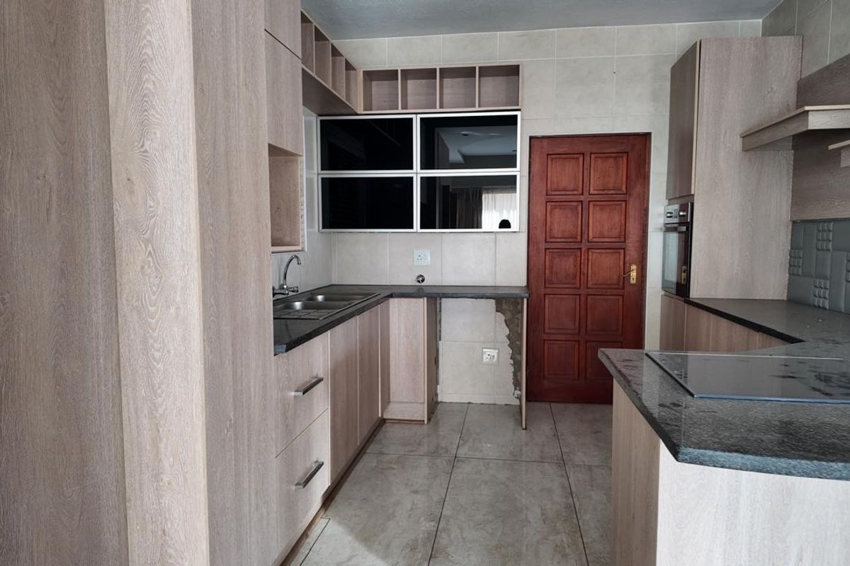 A functional kitchen featuring light wood-finish cabinetry, stone countertops, built-in oven, and hob, with tiled flooring and backsplash throughout.