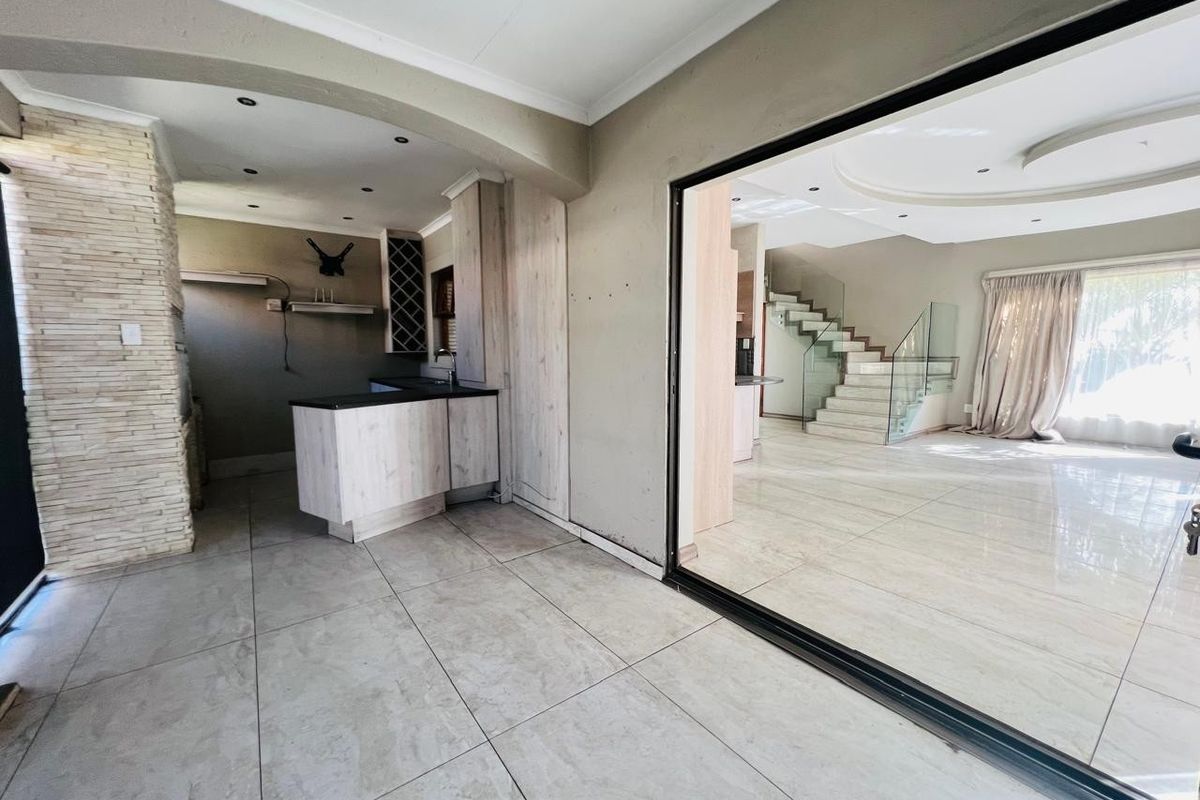 Spacious open-plan living area featuring large format floor tiles, a stone-clad feature wall, built-in cabinetry, and a modern staircase with glass balustrades.