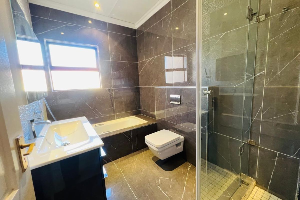 Modern bathroom featuring dark marble-look wall and floor tiles, a built-in bathtub, a wall-mounted toilet, and a separate glass-enclosed shower.