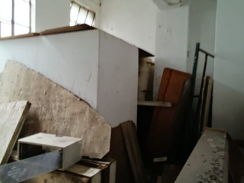 An interior utility or storage space showing significant signs of wear, peeling paint, and structural disrepair, currently filled with construction debris.