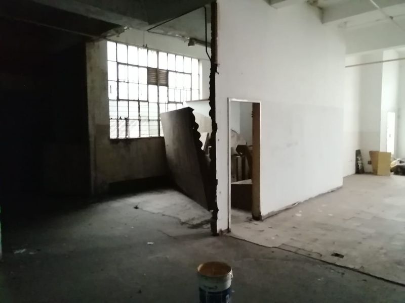 An expansive, industrial-style open plan commercial space featuring exposed concrete ceilings, large steel-framed windows, and unfinished wall surfaces requiring renovation.