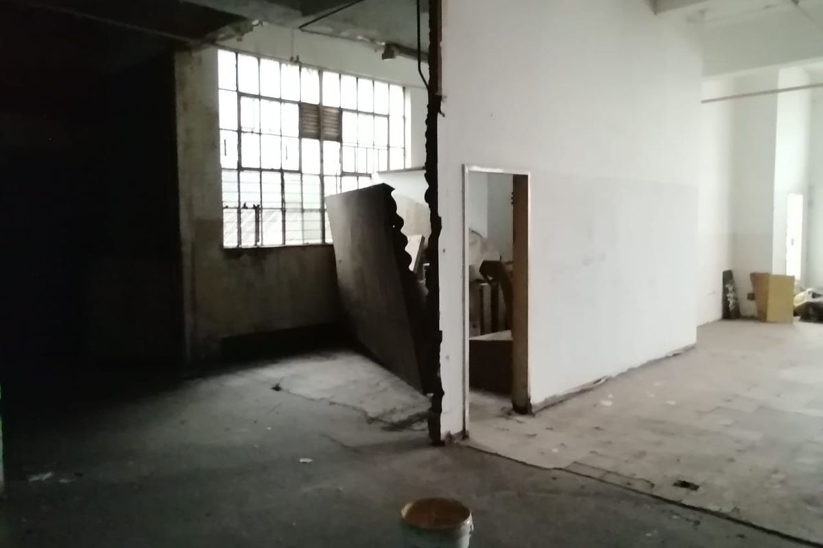 An expansive, industrial-style open plan commercial space featuring exposed concrete ceilings, large steel-framed windows, and unfinished wall surfaces requiring renovation.