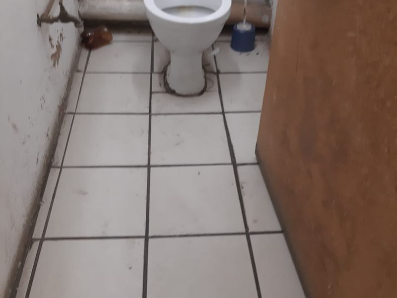 A small, functional bathroom featuring a standard toilet, tiled flooring, and exposed plumbing, currently requiring maintenance and cosmetic updates.