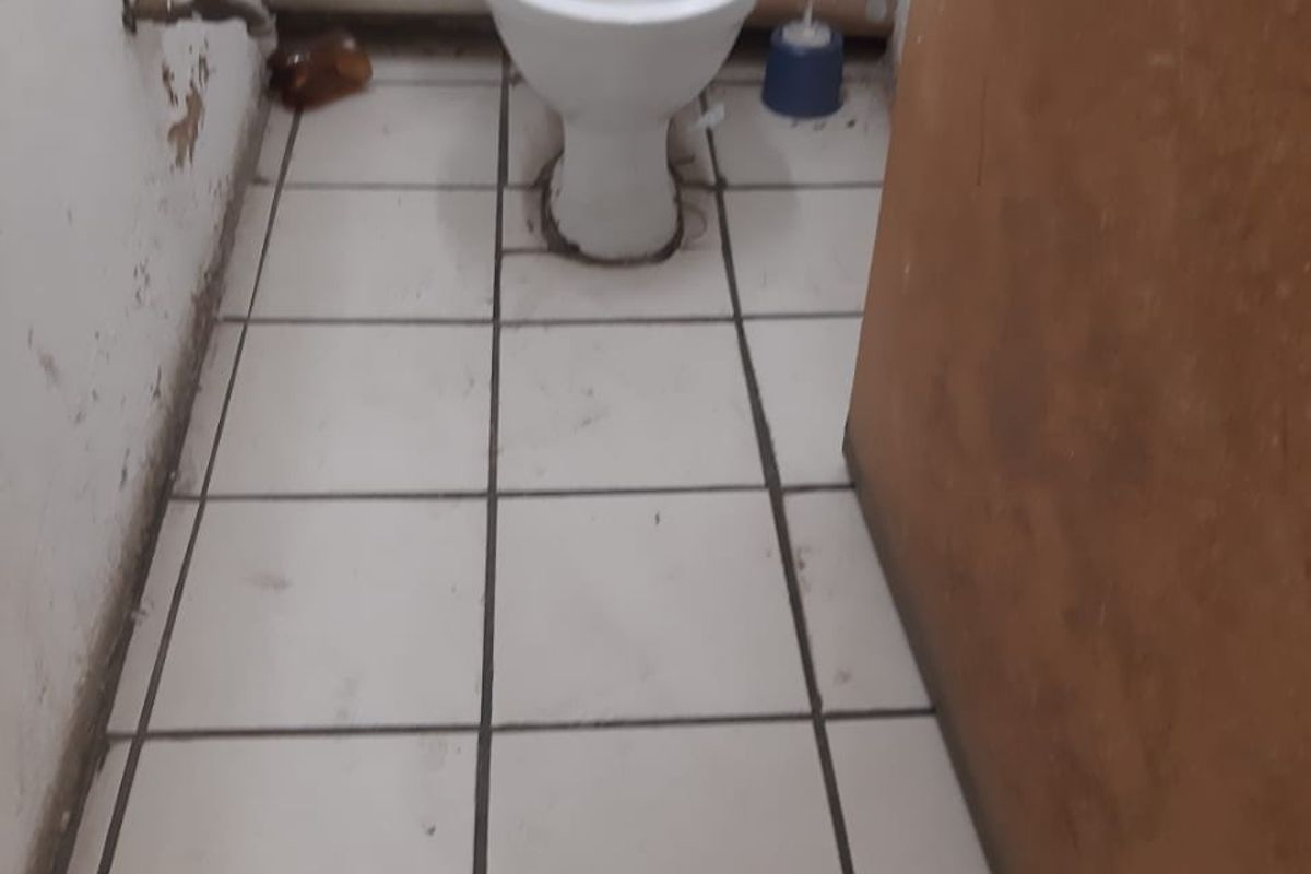 A small, functional bathroom featuring a standard toilet, tiled flooring, and exposed plumbing, currently requiring maintenance and cosmetic updates.