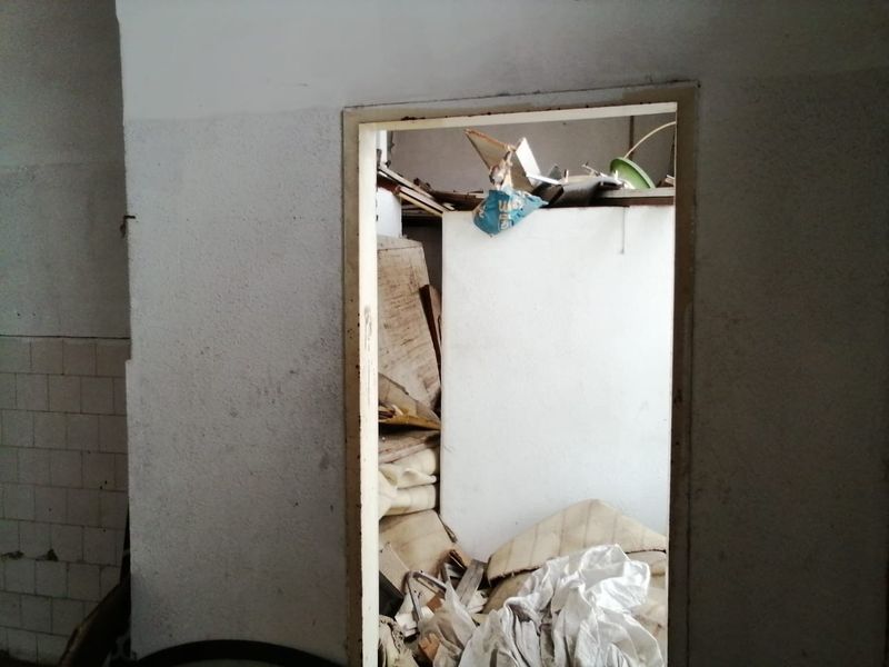 A small, dilapidated utility space or storage area showing significant wear, damaged wall finishes, and accumulated debris requiring renovation.