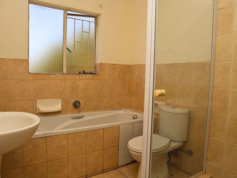 A functional bathroom featuring a pedestal basin, built-in bathtub, toilet, and a separate shower enclosure with tiled finishes throughout.