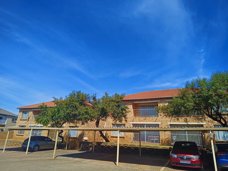 Exterior view of a face brick townhouse complex featuring covered parking bays and balcony access.