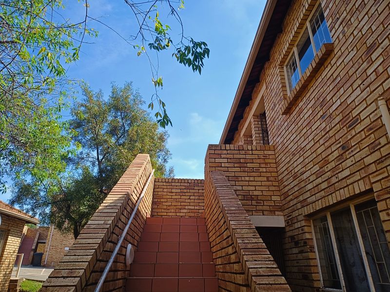 Exterior view of a townhouse featuring a face brick facade, a tiled staircase with a metal handrail, and aluminium window frames.