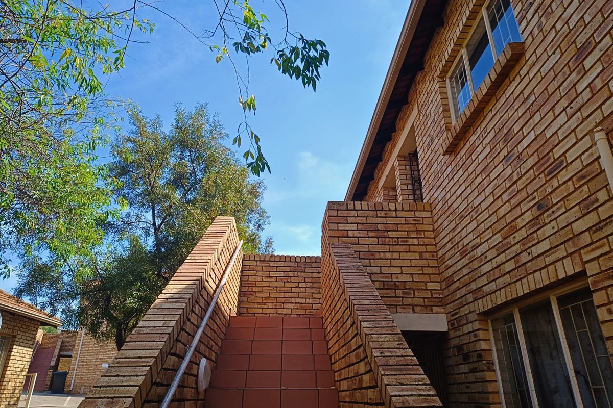 Exterior view of a townhouse featuring a face brick facade, a tiled staircase with a metal handrail, and aluminium window frames.