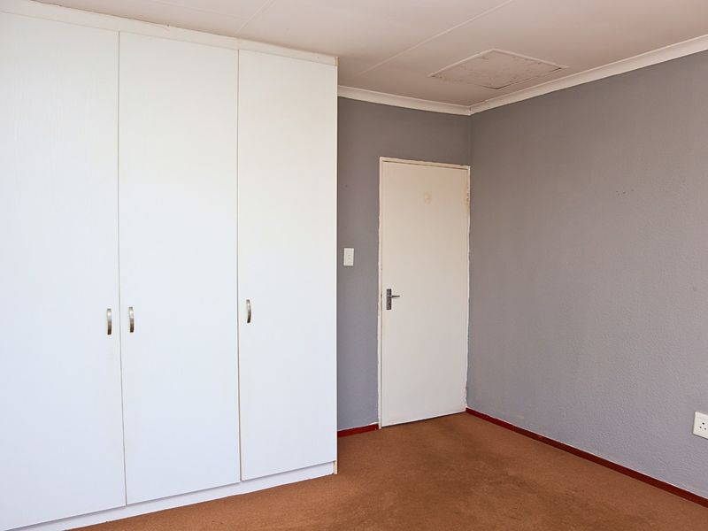 A vacant bedroom featuring built-in white cupboards, grey painted walls, and carpeted flooring, providing a blank canvas for potential interior design updates.
