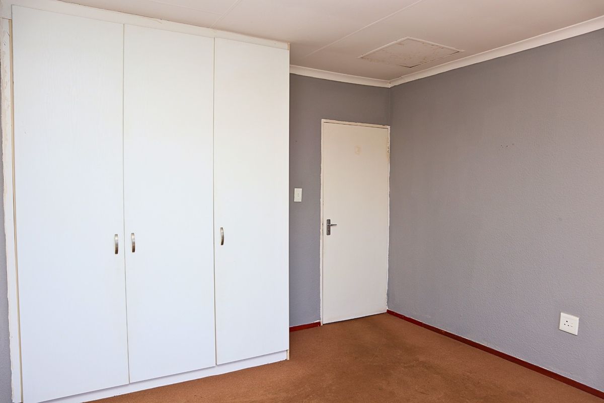 A vacant bedroom featuring built-in white cupboards, grey painted walls, and carpeted flooring, providing a blank canvas for potential interior design updates.