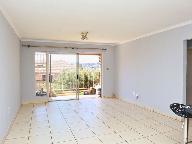 An empty, open-plan living area featuring tiled flooring and a sliding glass door that provides access to an outdoor balcony.