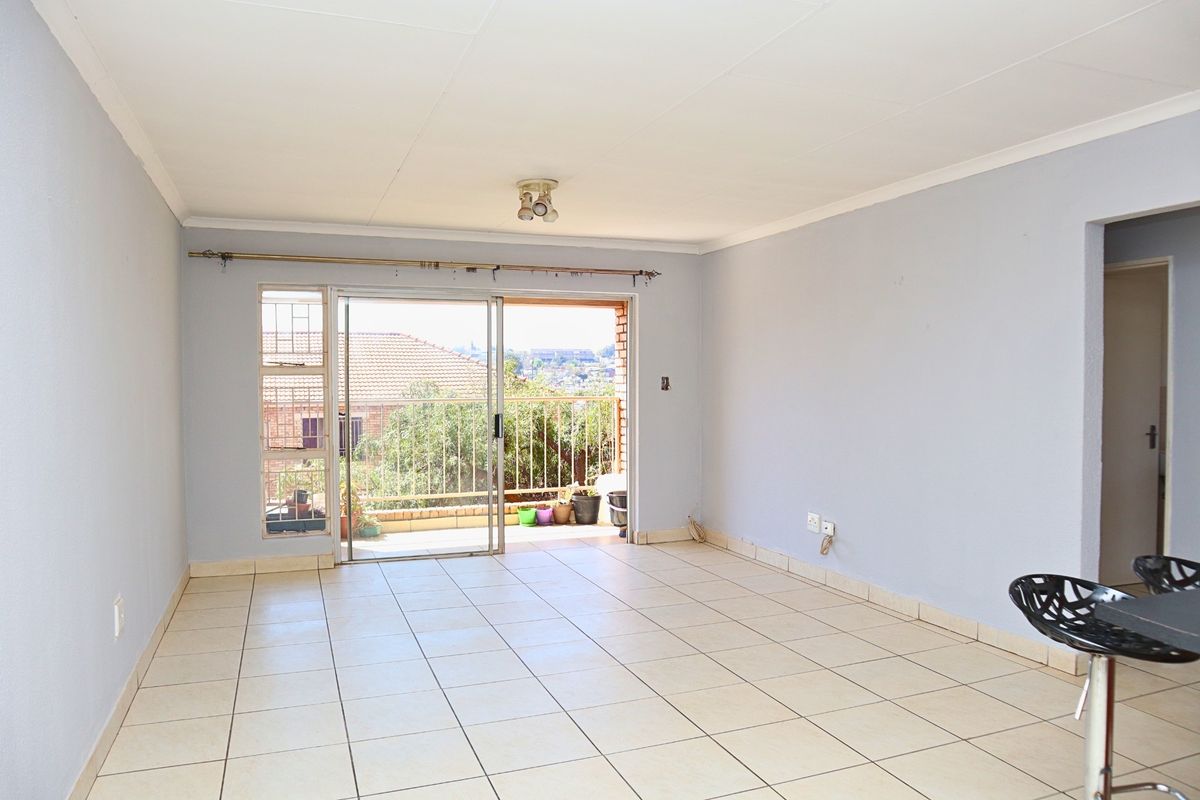 An empty, open-plan living area featuring tiled flooring and a sliding glass door that provides access to an outdoor balcony.