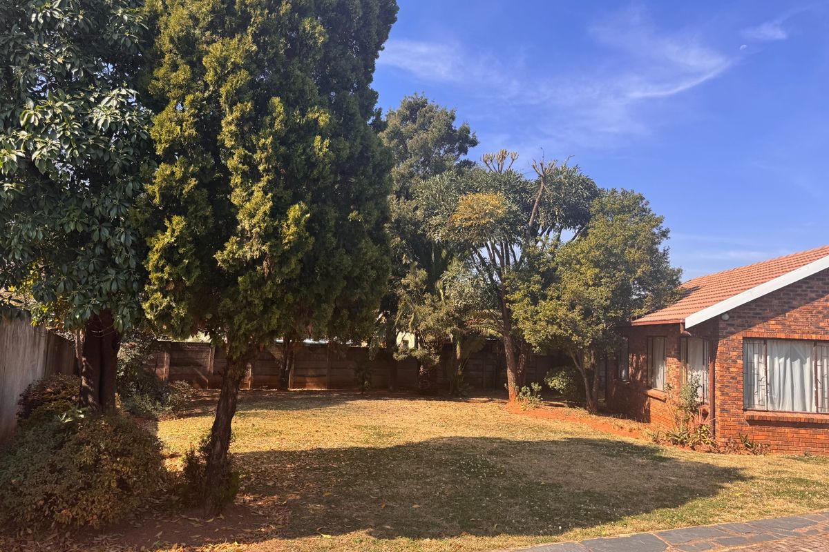 A spacious rear garden featuring a brick-faced house, mature trees, and a paved walkway, offering a private outdoor area with established landscaping.