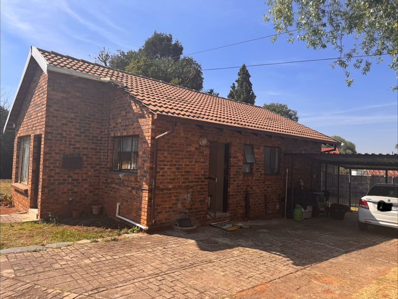 A single-story face brick house featuring a tiled roof, paved driveway, and an attached carport, presenting a classic residential exterior.