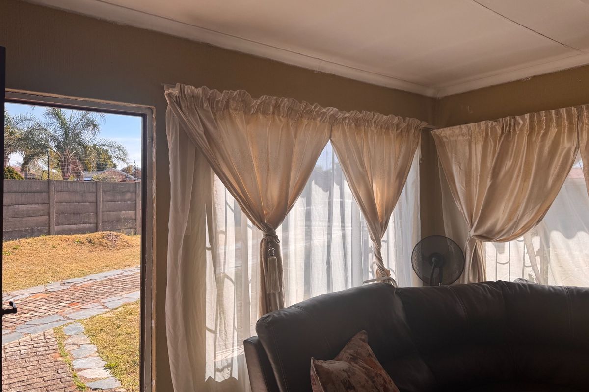 A living room area featuring natural light through large windows, with direct access to an outdoor paved walkway and garden area.