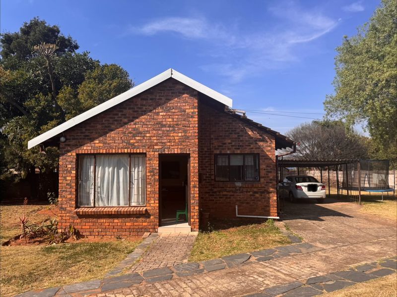 A single-story face brick house featuring a paved driveway, attached carport, and a front garden area.