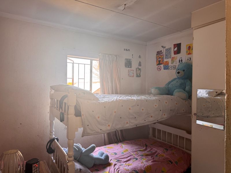 A bedroom featuring a built-in wardrobe and security bars on the window, requiring cosmetic updates to the wall and ceiling finishes.