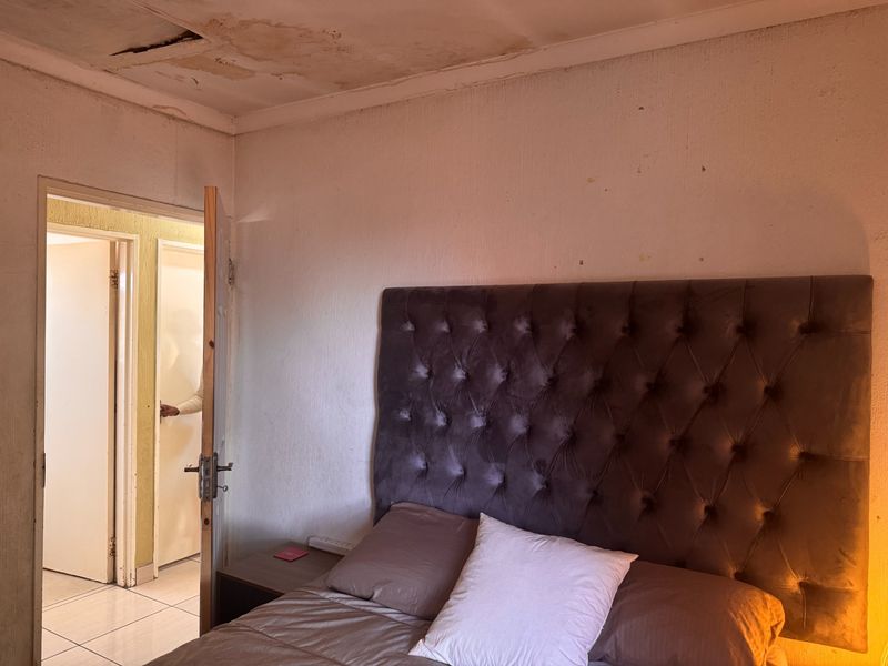 Bedroom featuring tiled flooring and access to an adjacent hallway, currently showing significant signs of ceiling water damage and plaster deterioration.