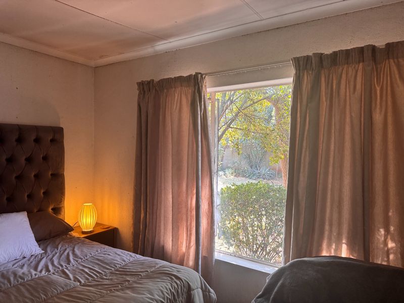 A bedroom featuring a window with garden views, requiring cosmetic updates to the walls and ceiling to improve the overall condition.