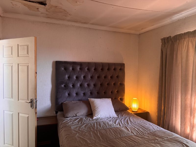 A bedroom featuring a panel door and ceiling cornice, currently showing significant signs of water damage and wear on the ceiling and walls.