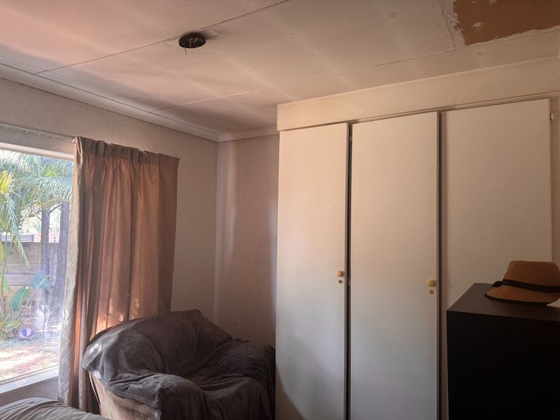 A bedroom featuring built-in cupboards and a sliding door, currently requiring ceiling repairs and cosmetic updates to improve the overall finish.