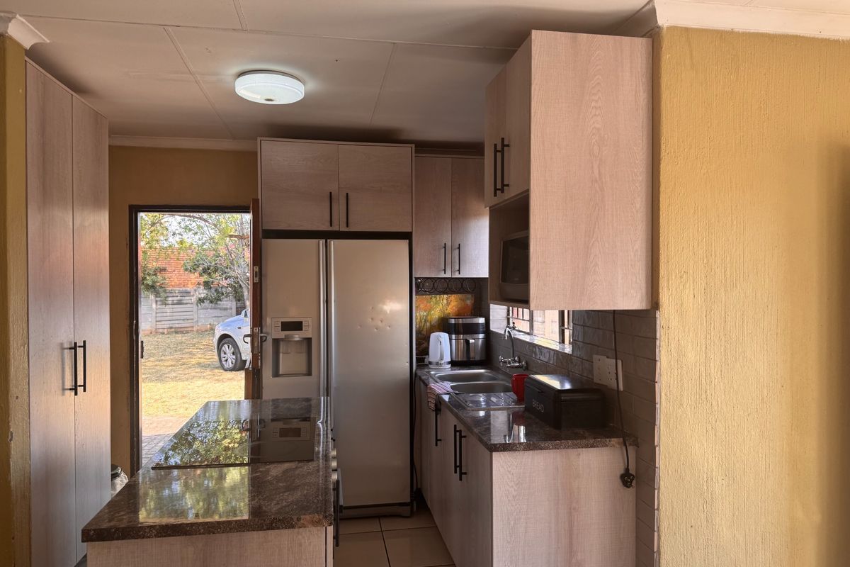 Functional kitchen featuring light wood cabinetry, granite countertops, a central island with a built-in hob, and direct access to the rear exterior.