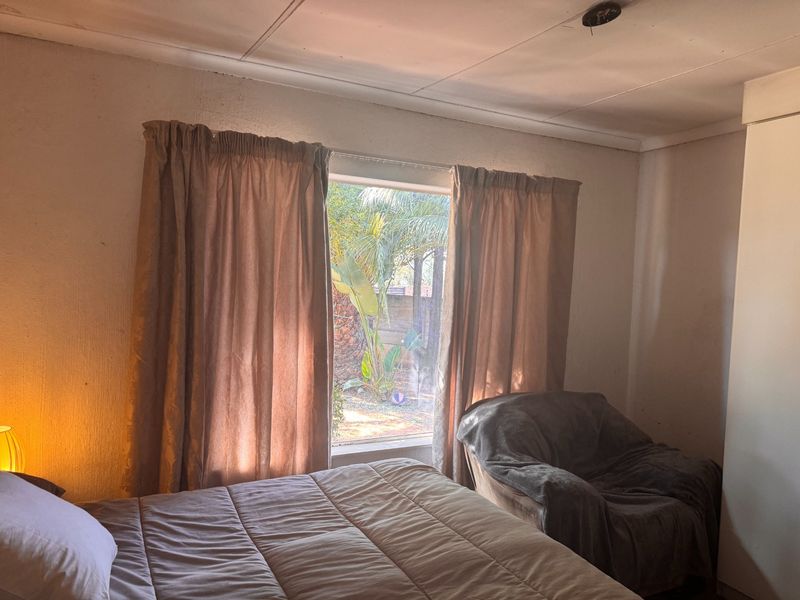 A bedroom featuring a built-in wardrobe and a window with garden views. The room requires cosmetic updates to the ceiling and wall finishes.