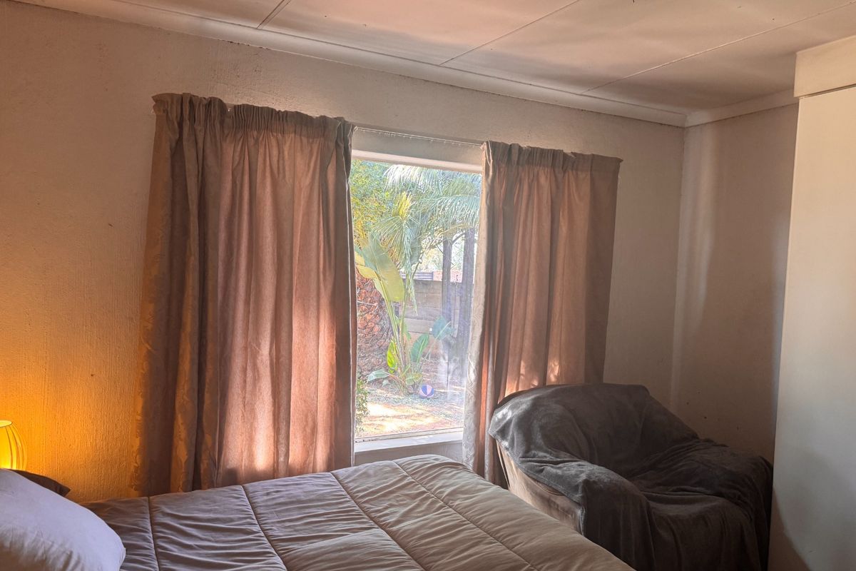 A bedroom featuring a built-in wardrobe and a window with garden views. The room requires cosmetic updates to the ceiling and wall finishes.