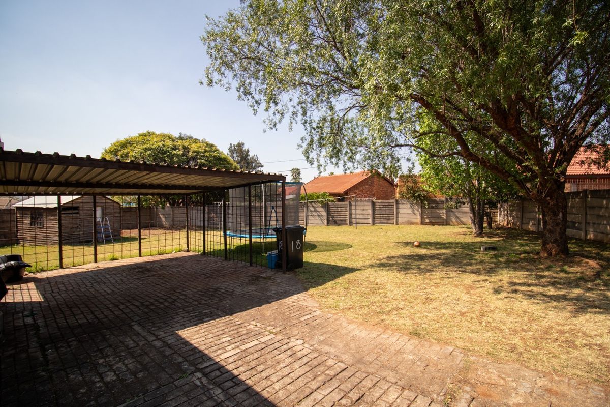 Spacious rear garden featuring a paved carport, mature trees, and perimeter precast concrete walling.
