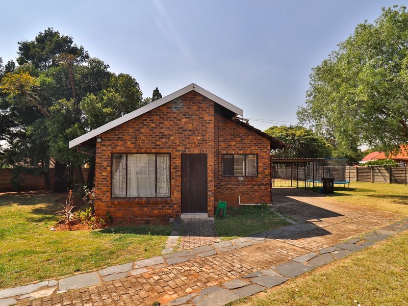 A single-story face brick house featuring a paved walkway, carport, and established garden setting.