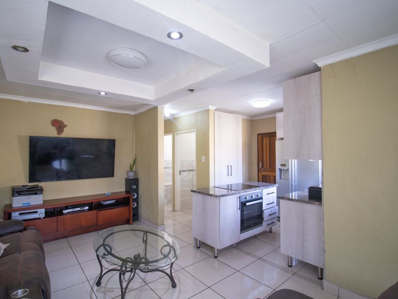 Open-plan living area featuring a kitchen with a central island, built-in oven, hob, and tiled flooring throughout, seamlessly connecting to the lounge space.
