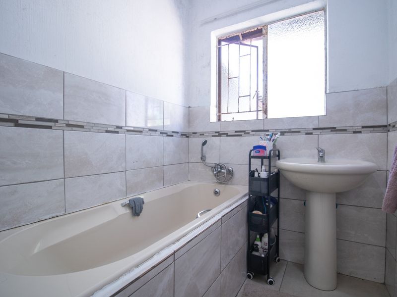 A functional bathroom featuring a bathtub, pedestal basin, and tiled wall finishes, requiring some maintenance to the window frame and fixtures.