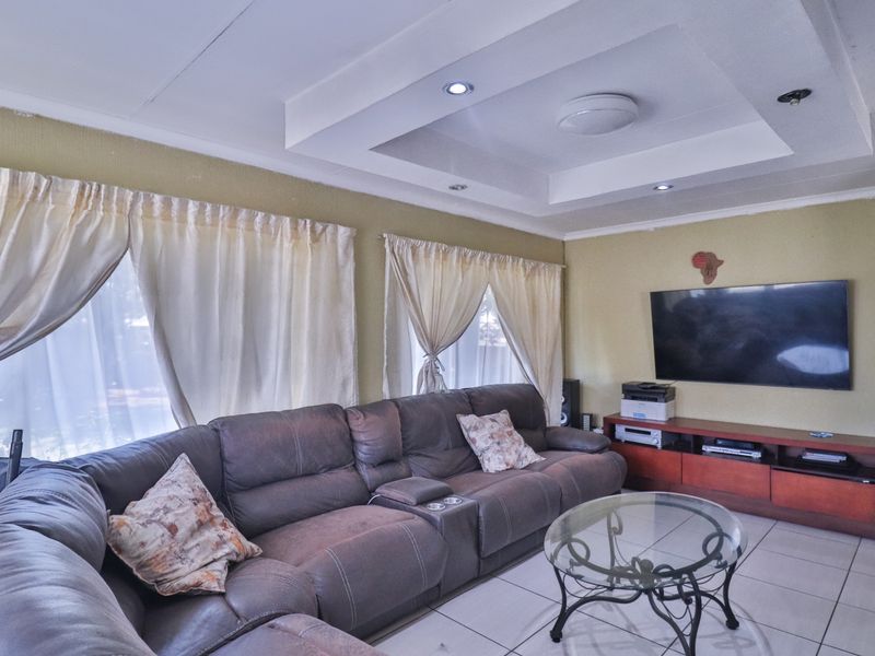 A comfortable living room featuring a recessed ceiling with downlights and neutral tiled flooring.