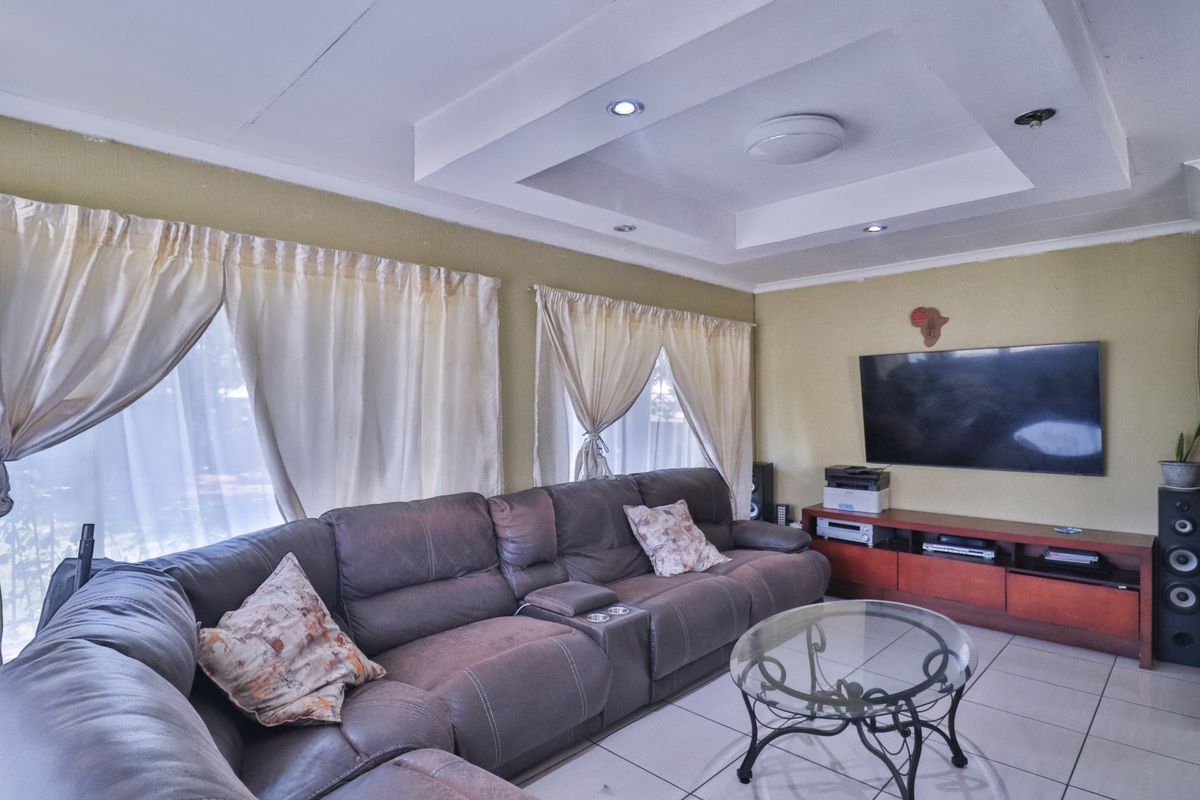 A comfortable living room featuring a recessed ceiling with downlights and neutral tiled flooring.
