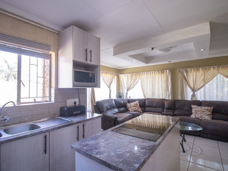 Open-plan kitchen and living area featuring modern cabinetry, a central island with an integrated hob, tiled flooring, and recessed ceiling lighting.