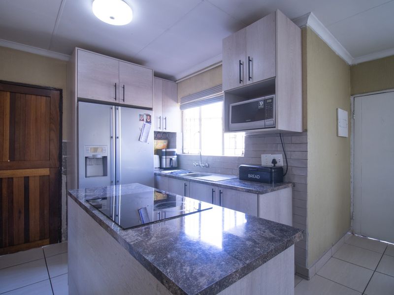 A functional kitchen featuring light-toned cabinetry, granite countertops, a central island with an integrated hob, and tiled flooring.